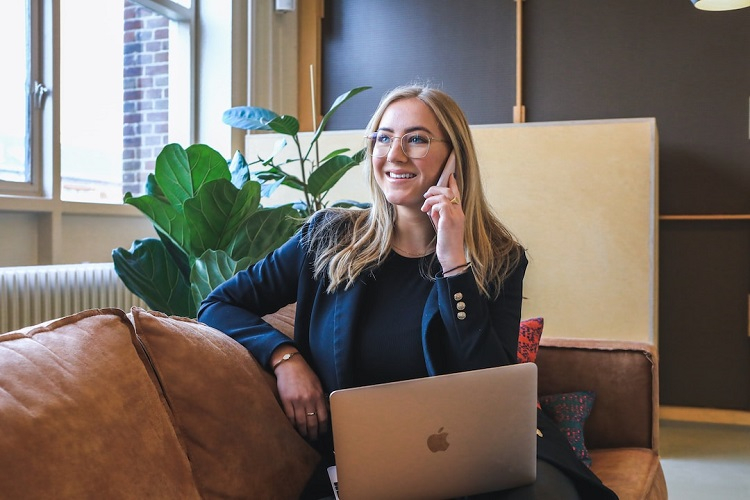 Businesswoman sitting on brown couch with laptop going over donut chart and bar graph